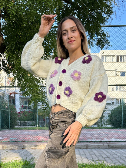 

bone-colored cardigan, violet flower cardigan, cozy knitwear, floral knit cardigan, soft yarn cardigan, elegant layering piece, feminine cardigan, stylish fall sweater, delicate floral details, comfortable fashion